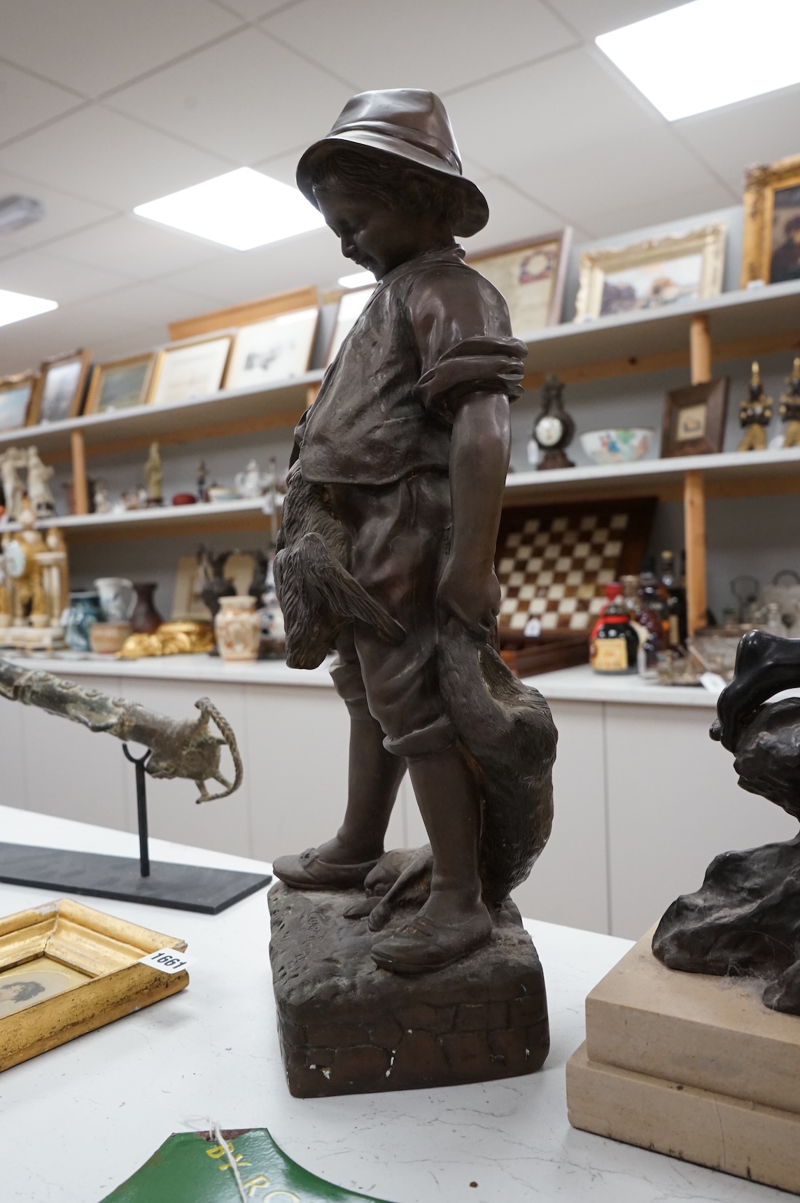 A bronze figure of a young boy carrying dead game, signed August, and a classic bronze of a young boy holding a fish, indistinctly signed, largest 53cm high